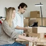 Business partners organizing inventory in an online store setup with clothes and boxes.