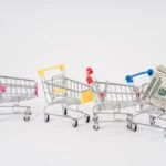 Miniature shopping carts in bright colors with dollar bills imply financial shopping themes.