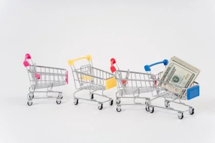 Miniature shopping carts in bright colors with dollar bills imply financial shopping themes.