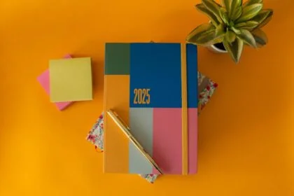 Flat lay of a vibrant 2025 planner with a pen and green plant on yellow background.