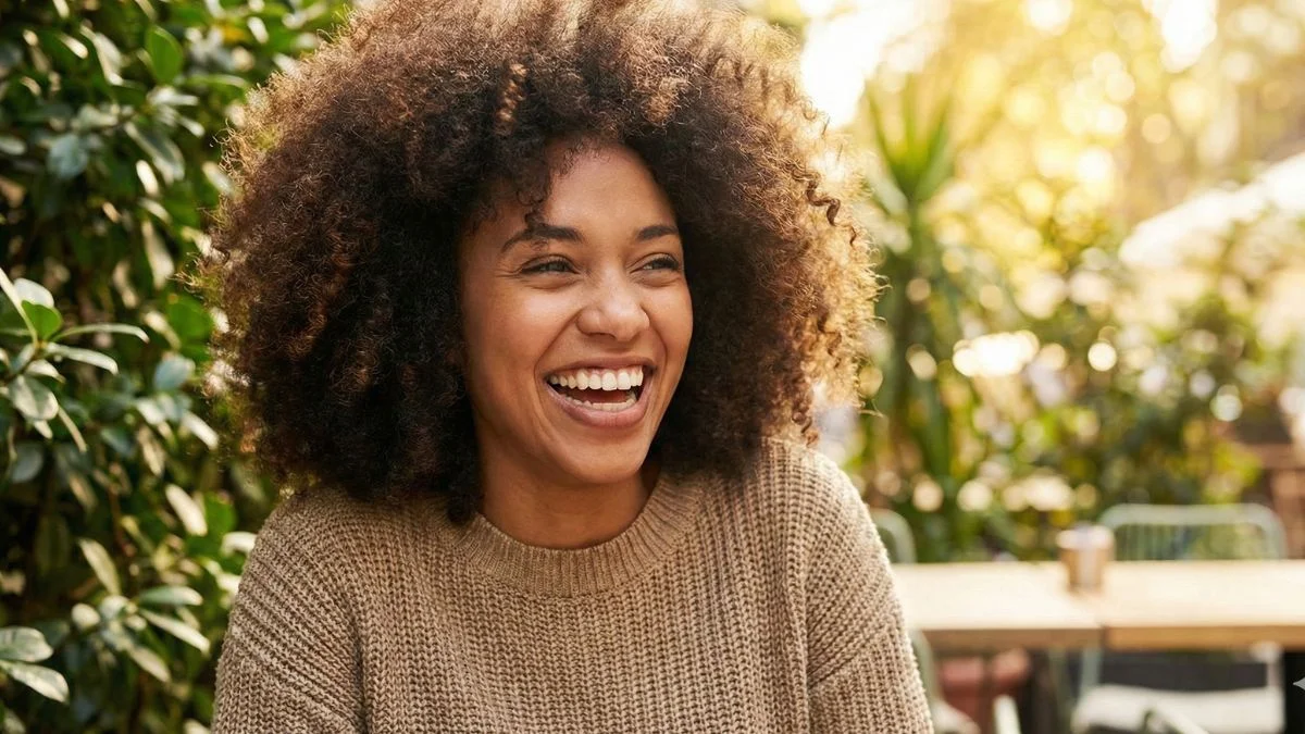 oto de close-up de uma mulher negra sorrindo, com cabelos cacheados volumosos, brilhantes e perfeitamente definidos. Representa o resultado dos melhores produtos para cabelos cacheados.