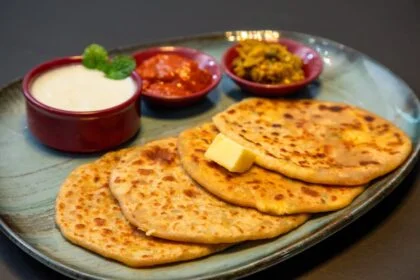 Appetizing Indian paratha served with yogurt and pickles on a blue plate.