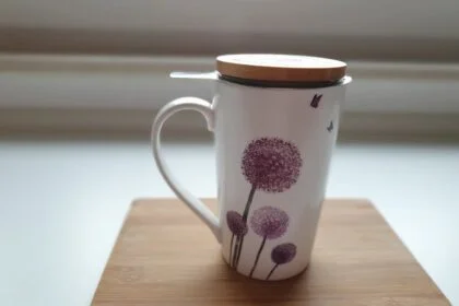 Elegant ceramic cup with lid, featuring purple floral design, on a wooden board.