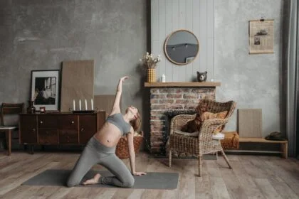 Pregnant woman practicing yoga near a fireplace with a dog in a cozy room.