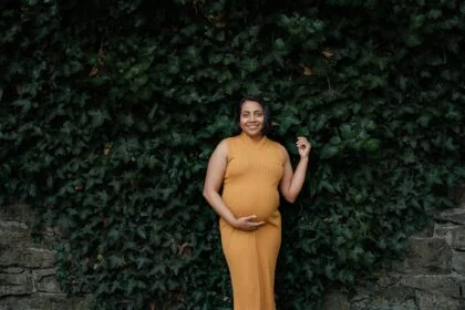 Maternity photo of a woman in autumn, wearing a mustard dress against a leafy backdrop.