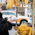 A woman selects grilled corn from a vibrant street food stall. Urban setting with outdoor atmosphere.